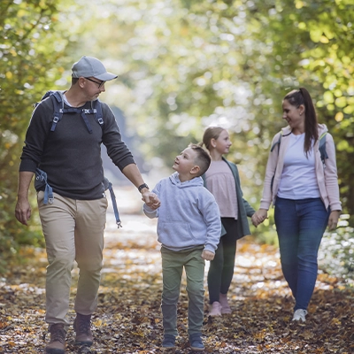 A family goes for a walk on a leaf-covered trail in the woods. 