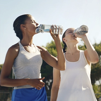 Two women wearing activewear drink water after exercising.