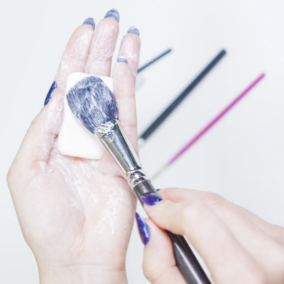 Hands cleaning a makeup brush with a small bar of soap.