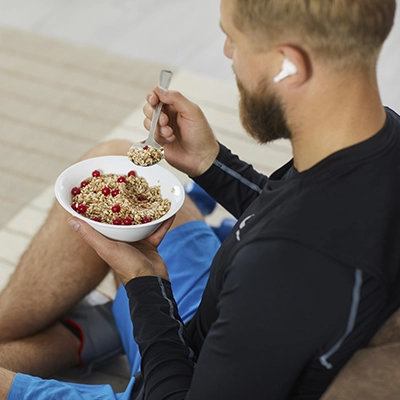 A man sits on the floor eating a bowl of cereal with berries. 