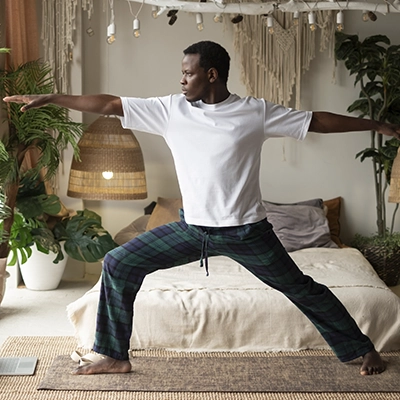 A man does the warrior yoga pose in his bedroom. 
