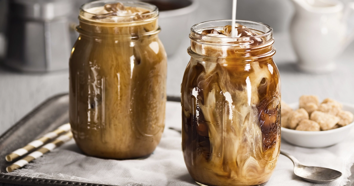 Milk being poured into iced coffee in a clear jar.