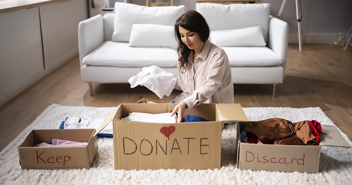 Woman sorting items in three boxes labeled keep, donate, and discard.
