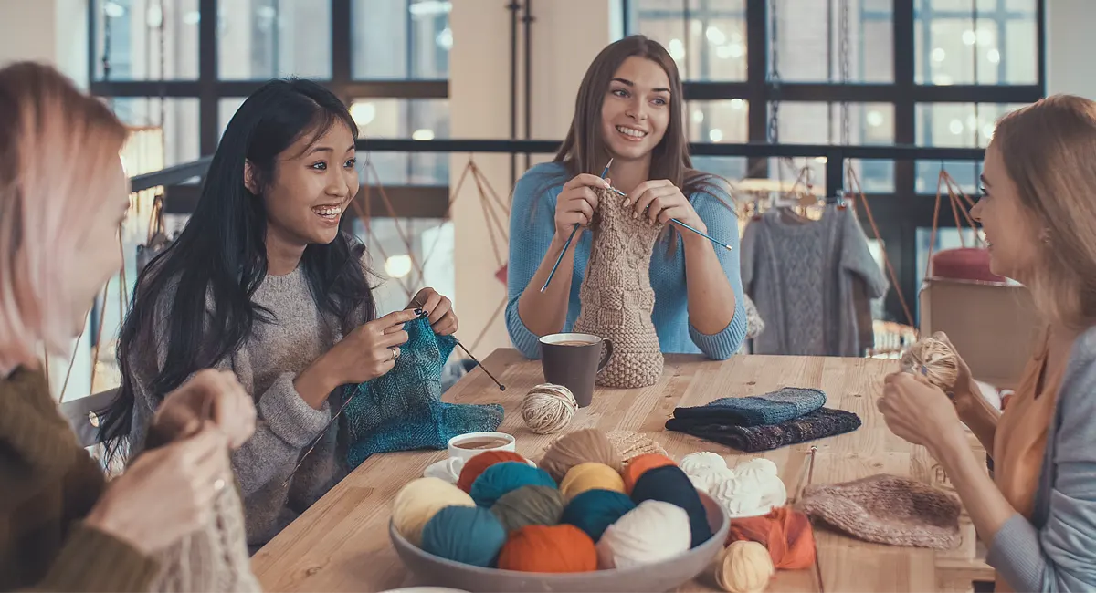 Women sit around a table while knitting. 