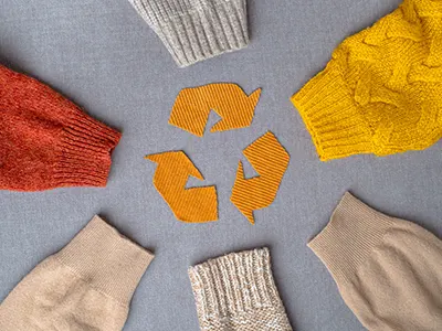 knitted sleeves of different yarns and patterns encircle a recycle symbol made of cut out yellow fabric. 