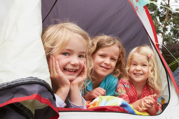 Three girls in a tent smile at the camera.