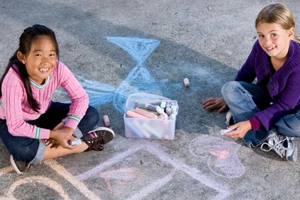 Two girls draw outside with sidewalk chalk. 
