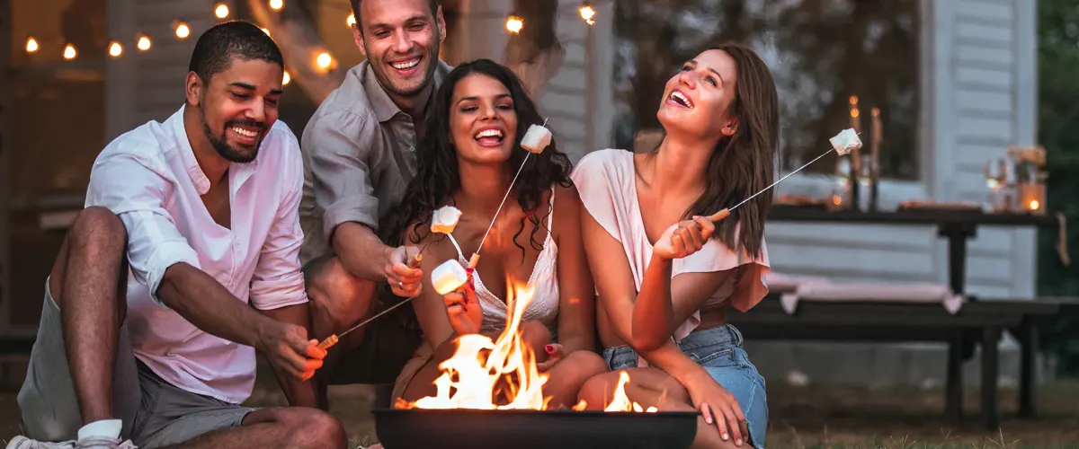 Friends toast marshmallows outside by a fire pit.