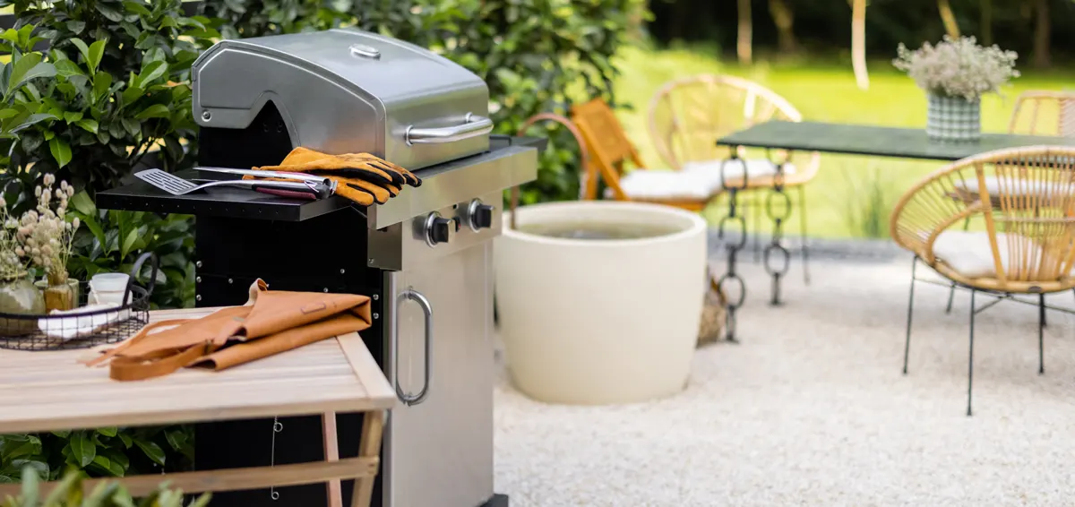 A stainless steel gas grill sits on a patio next to a small wooden table