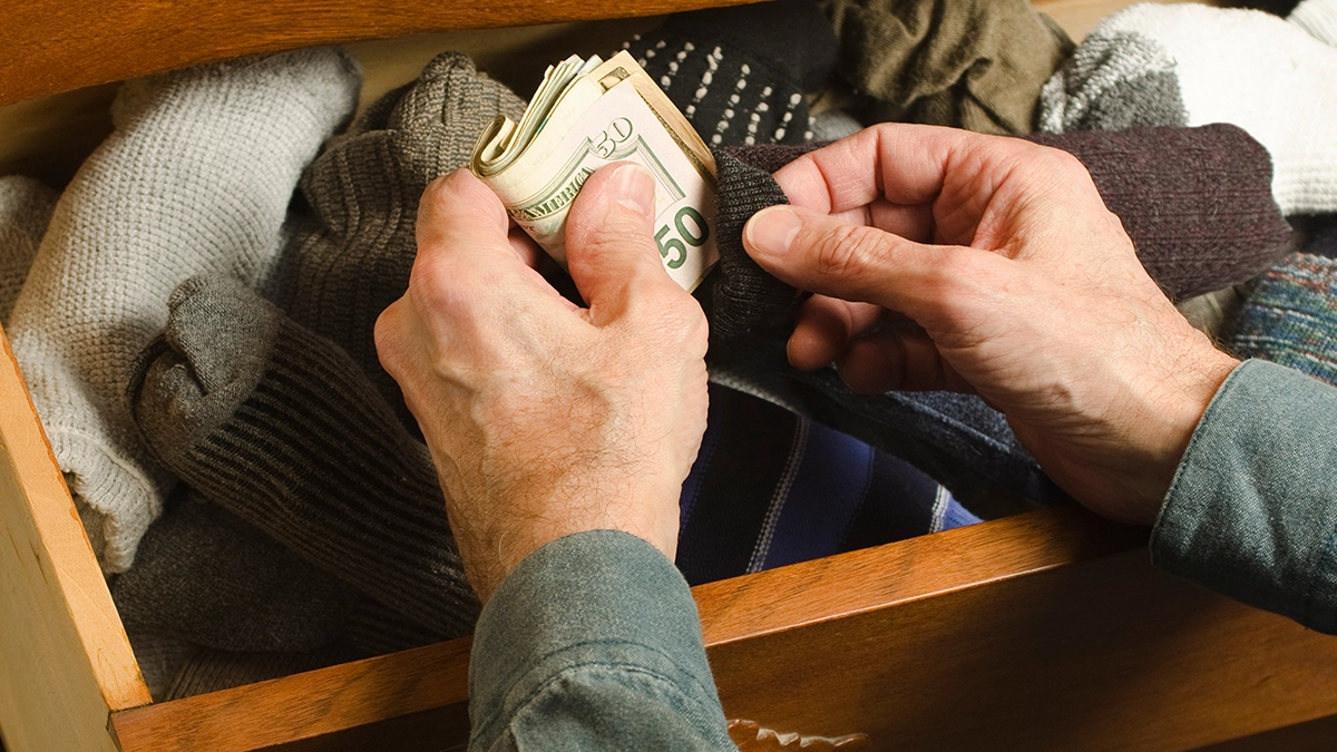 A man tucks money into a sock in his sock drawer
