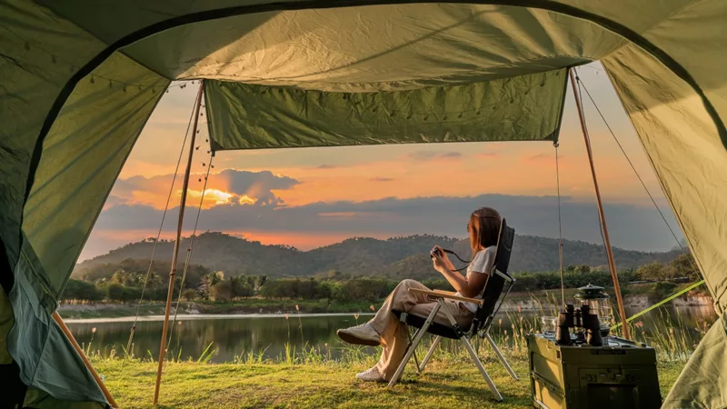 Woman sitting on folding chair outside of tent overlooking scenic view