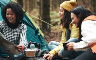 Three people gather near a tent in the woods to look at a map.