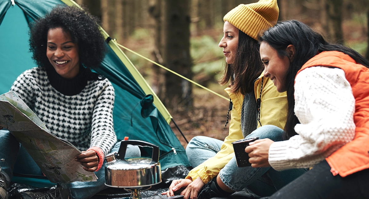 Three people gather near a tent in the woods to look at a map.