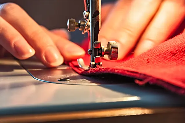 A close-up of a woman's hands sewing red fabric on a sewing machine.