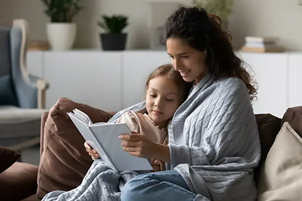 A mother and daughter read together while wrapped in a blanket.