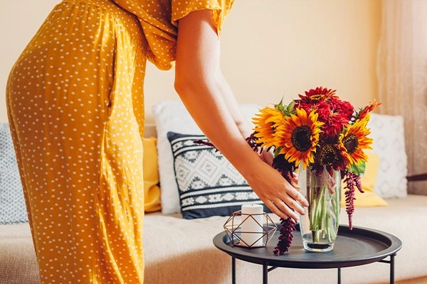 A person places a fall-themed floral arrangement with sunflowers on a table.