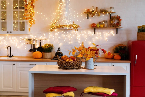 A kitchen is filled with gourds, autumn leaves, and string lights.