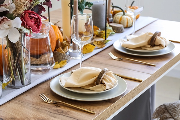 A fall-themed dinner table is set with pumpkins, candles and fall leaves.