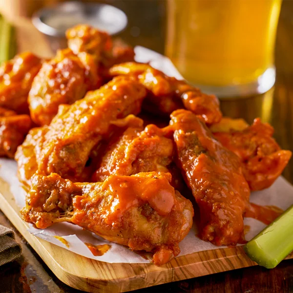 Buffalo sauced chicken wings on wooden board with celery.