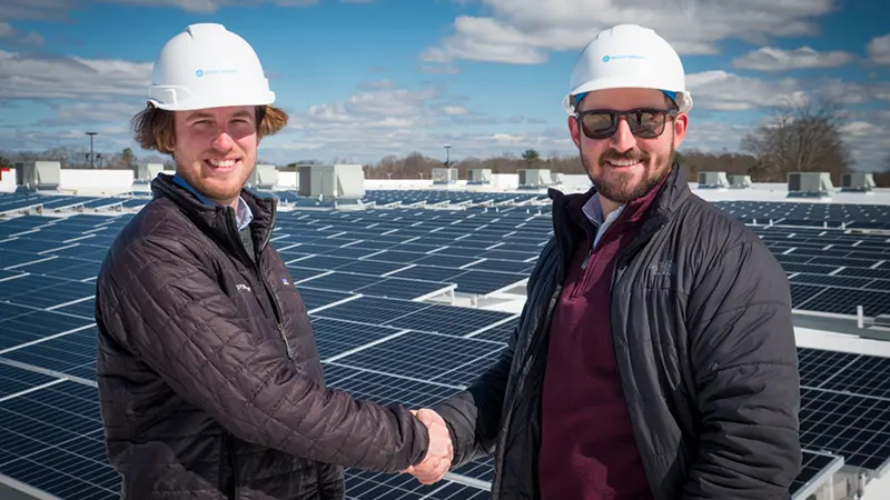 Two men on a roof shaking hands after rooftop solar installation