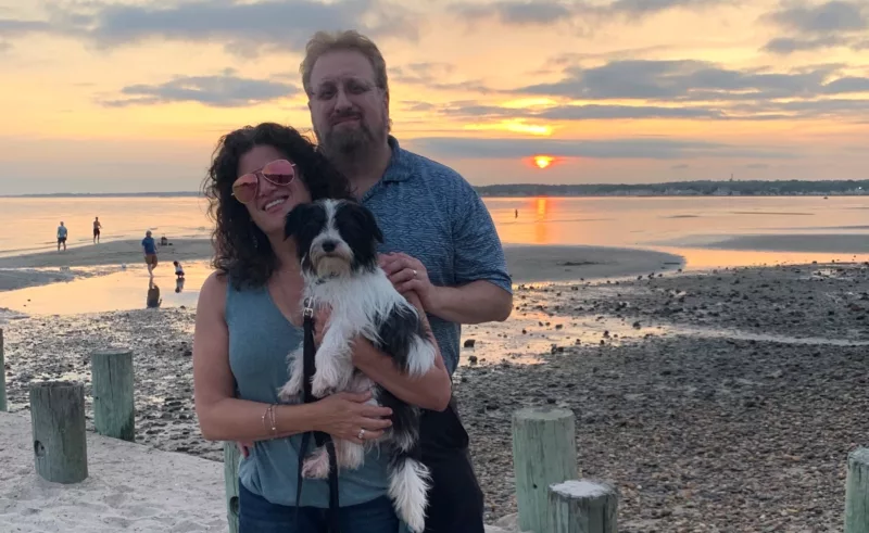 Two people with a rescue dog at the beach during sunset.
