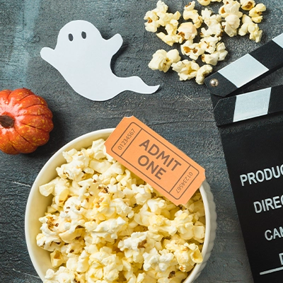 Bowl of popcorn on a table next to halloween decor and film slate.