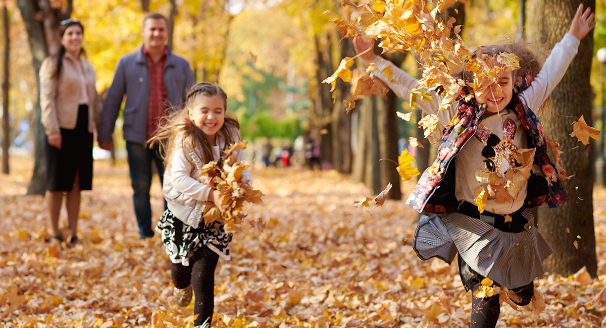 Parents watch kids throwing leaves into the air