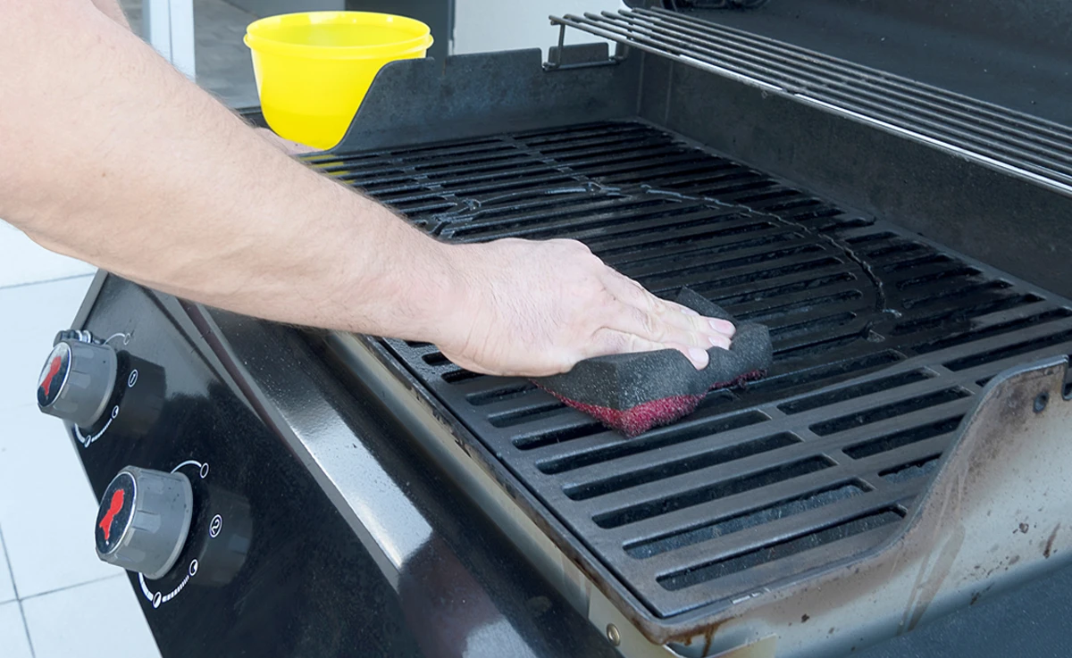 Man cleaning grill with sponge