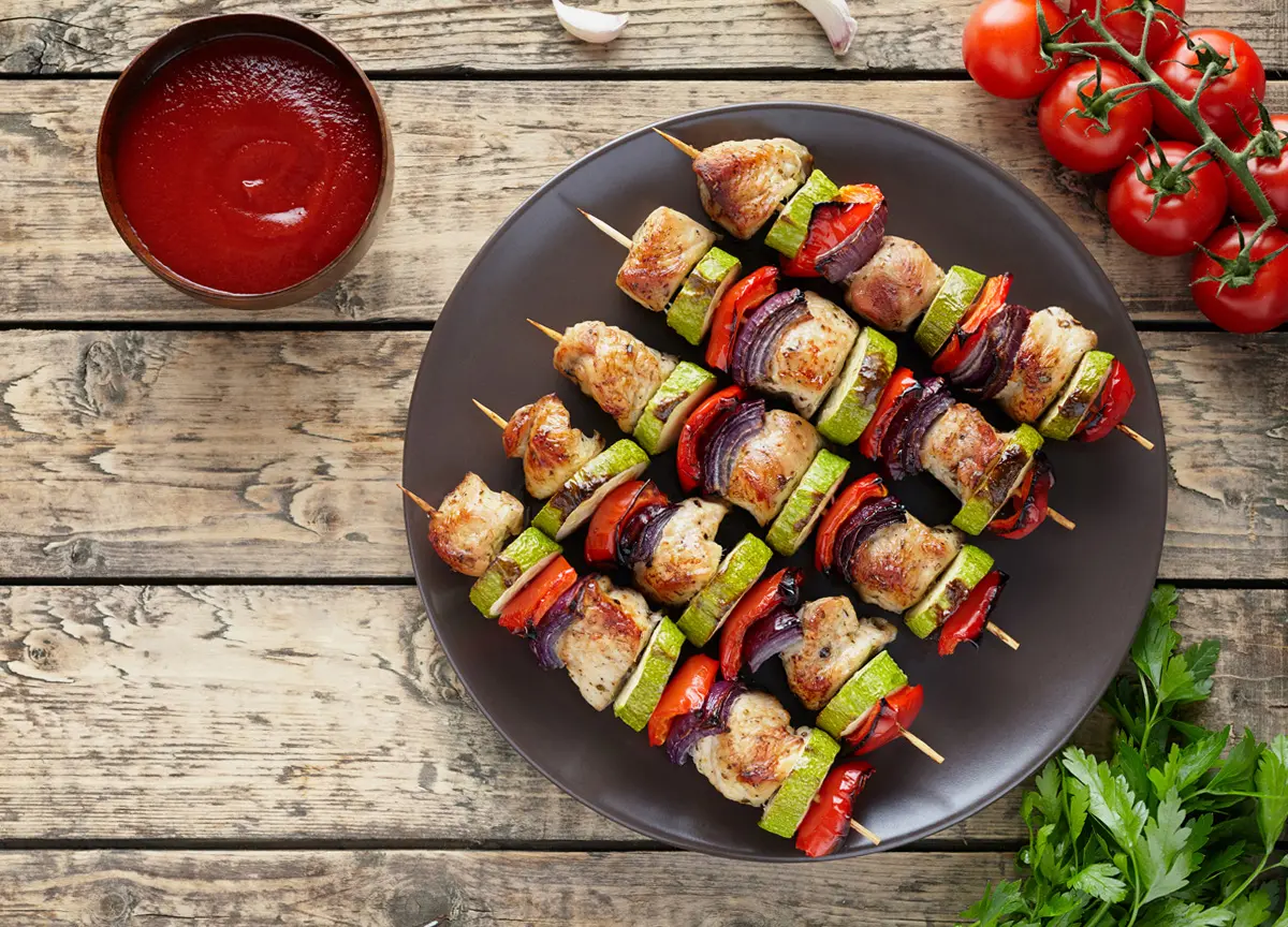 Top view of grilled turkey and vegetable skewers on a black plate.