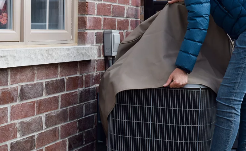 person placing cover on outdoor air conditioning unit