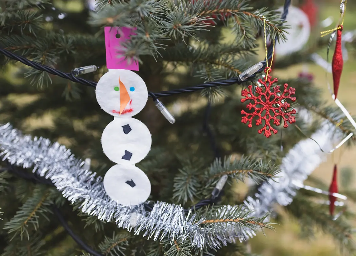 A snowman made from round cotton pads on a decorated Christmas tree.