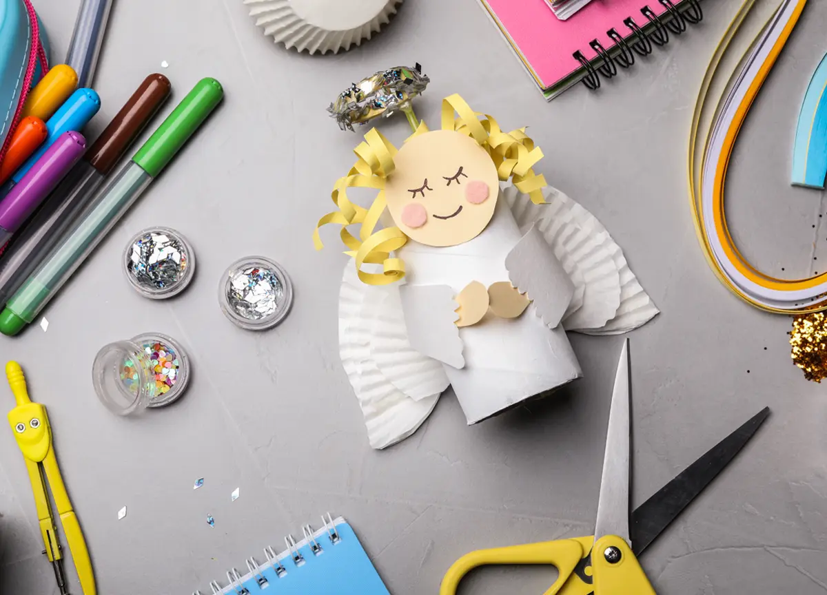 A paper angel and crafting supplies sit on a table.