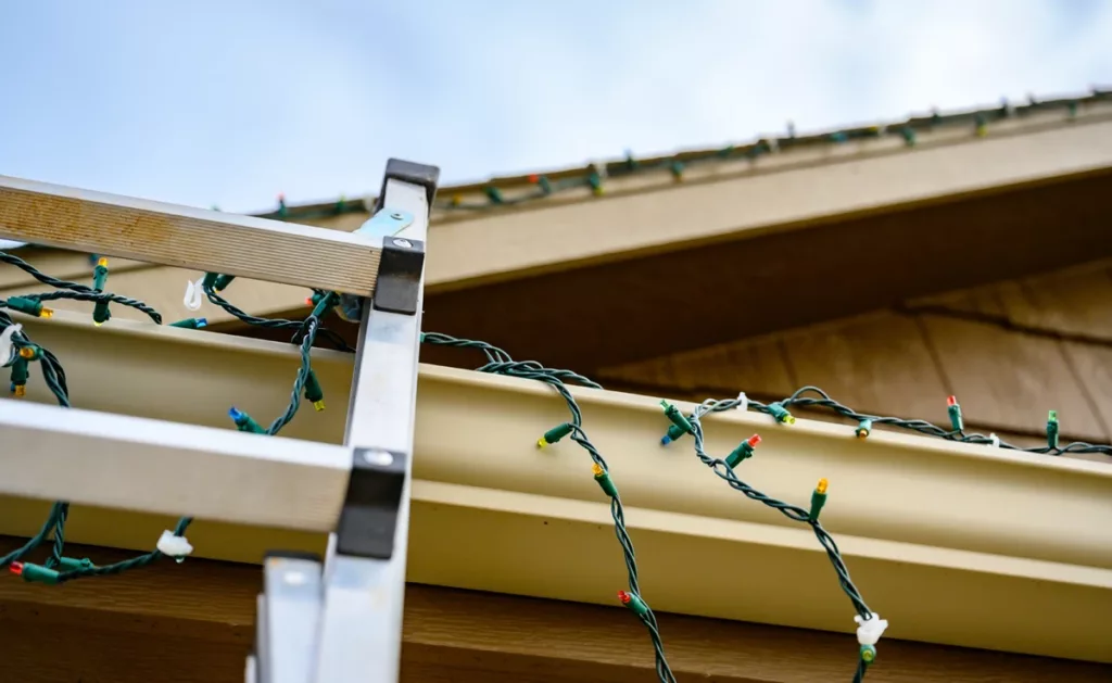 Christmas lights being hung along the roof line and gutters.