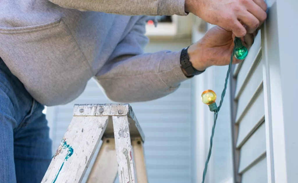 Man putting up Christmas lights outside of home
