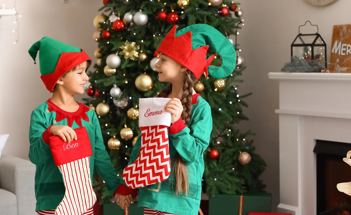 A boy and girl dressed as Christmas elves pose with their Christmas stockings.