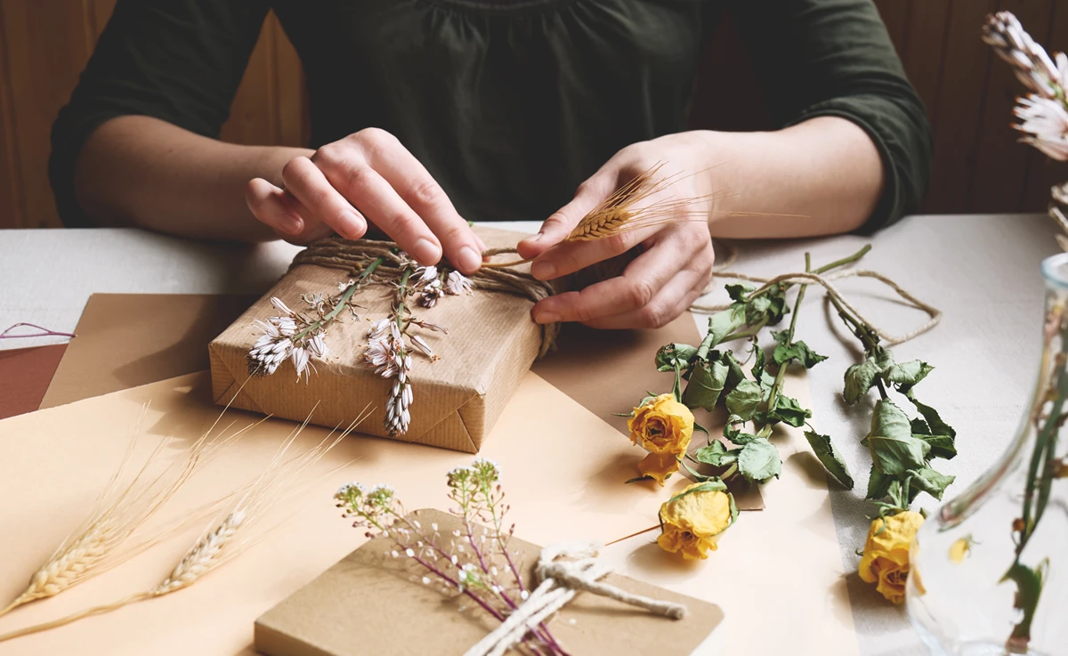 A woman tucks dried flowers into a hand-wrapped gift.