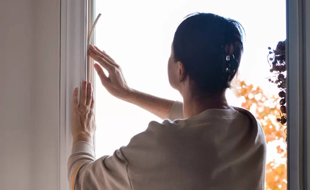 A woman putting up weather stripping on the door.