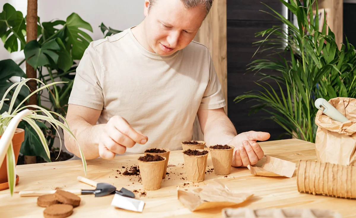 A man places seeds in seed starter pots.