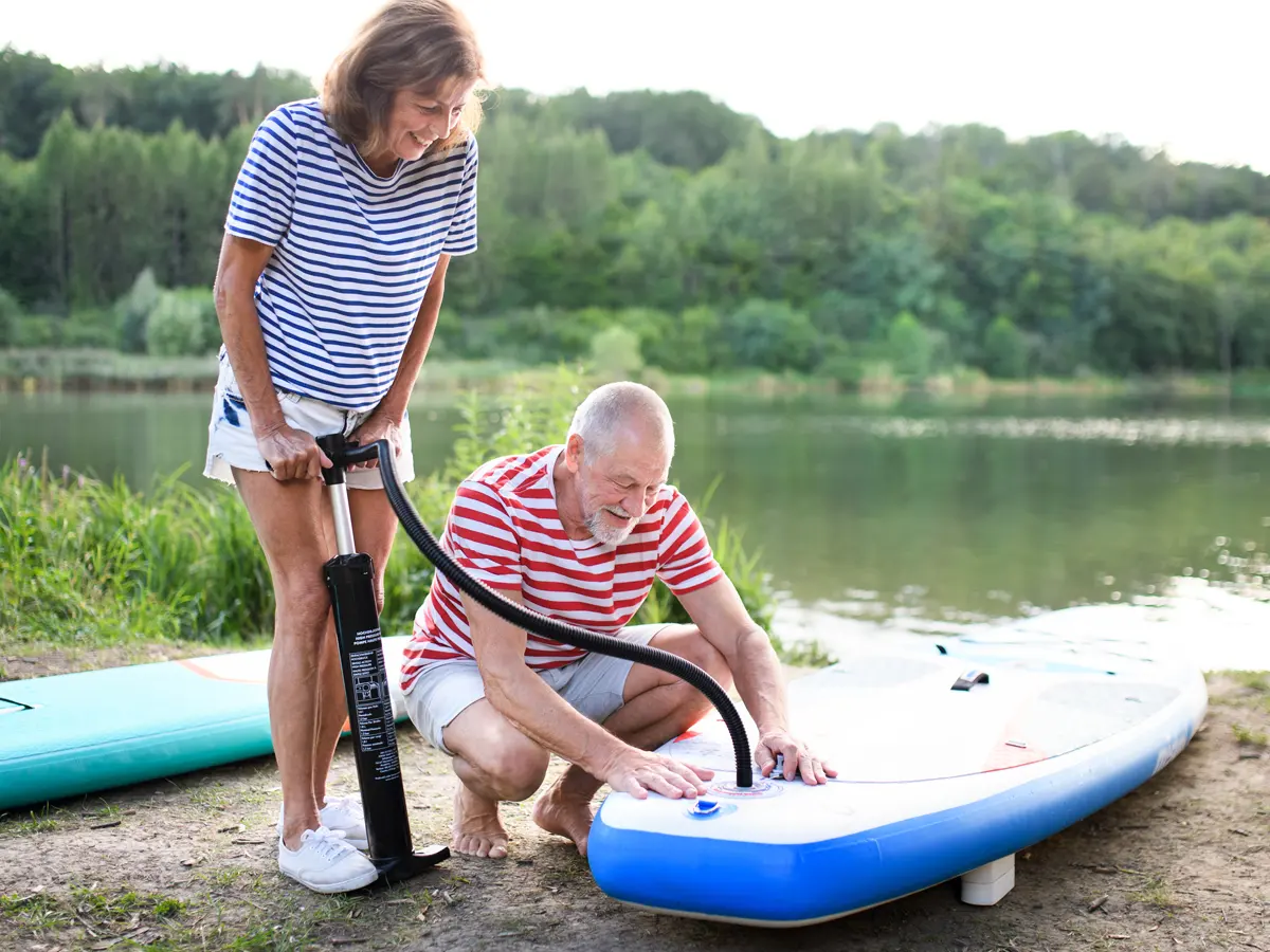 A couple inflates a paddleboard on the lakeshore.
