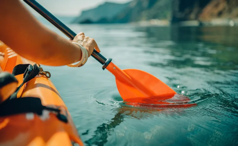 A close-up of a kayak paddle being dipped into the water.