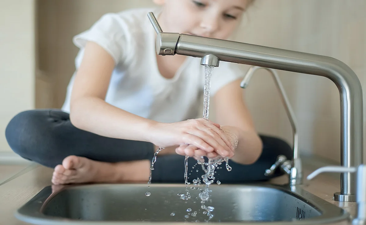 A little girl washing hands using less water being eco-friendly.