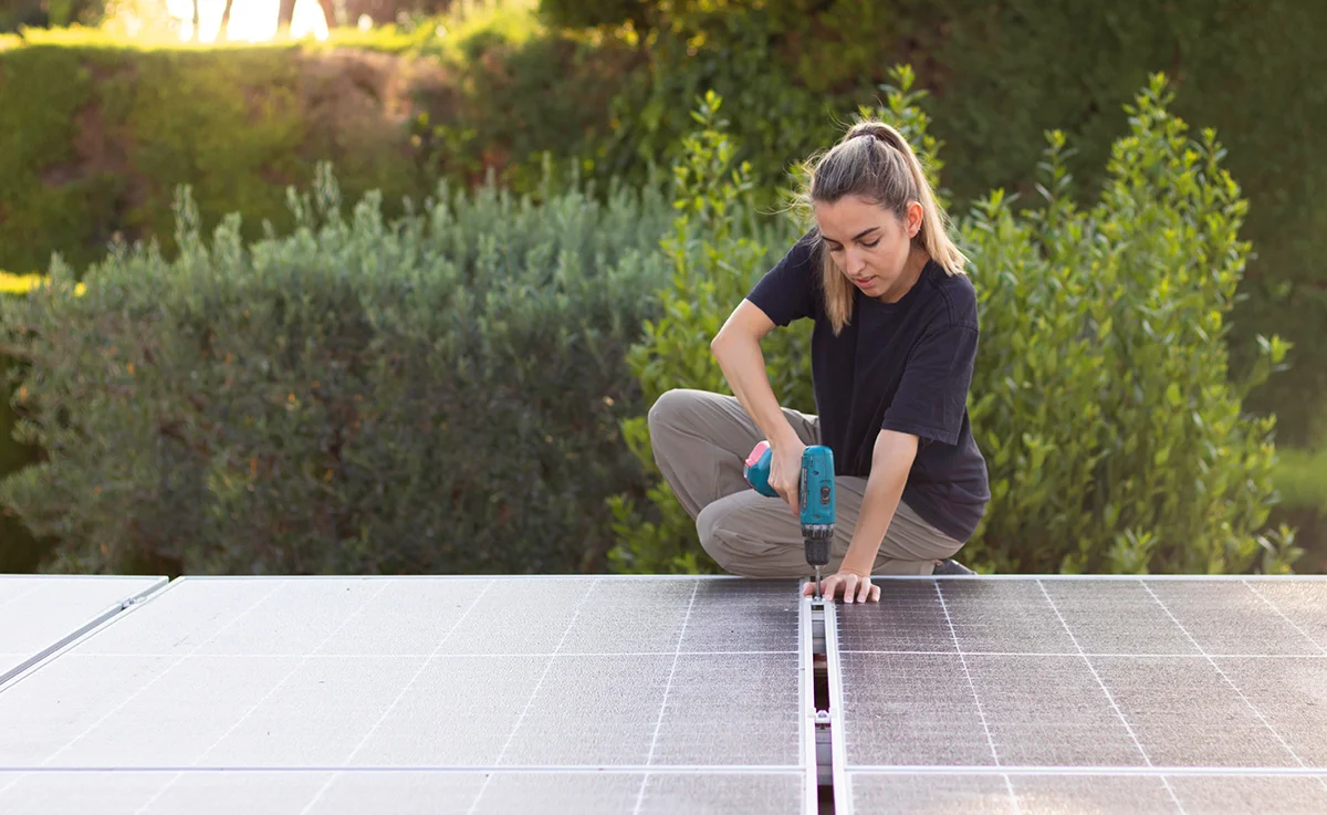 Young woman working on a solar panel installation to get renewable energy with garden in the background