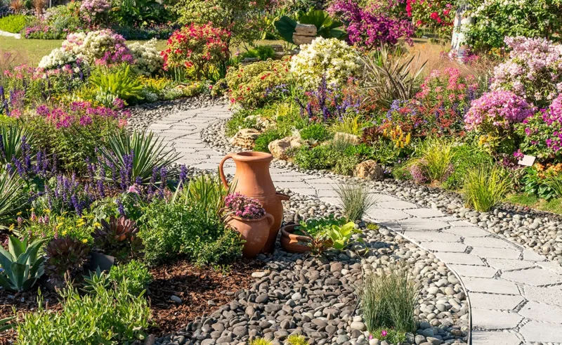 A stone path winds through flowers and brightly colored ornamental grasses.