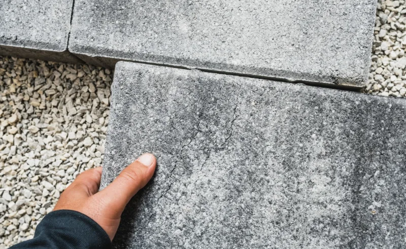 A close-up of a hand installing pavers over gravel.