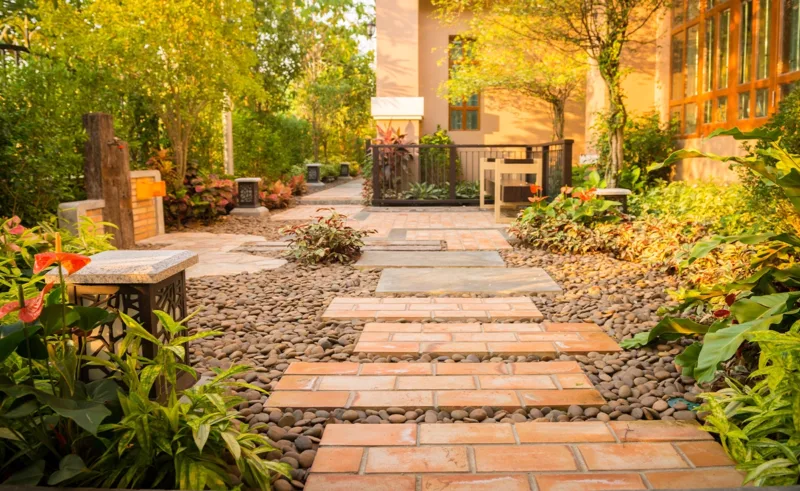 Brick pavers over stones create a walkway through a backyard.