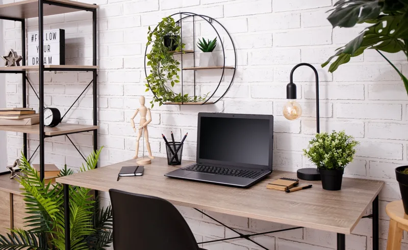 A neatly organized desk with some personal touches like plants, a drawing mannequin, and a contemporary desk lamp.