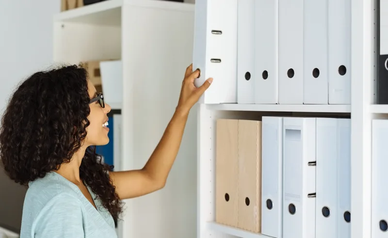 A person removes a file from a shelf of neatly organized files.