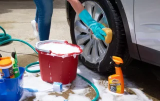 A person washing the wheels of a car with soap.