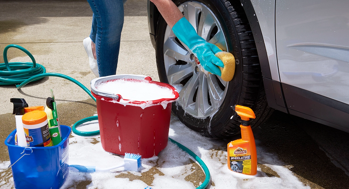 A person washing the wheels of a car with soap.