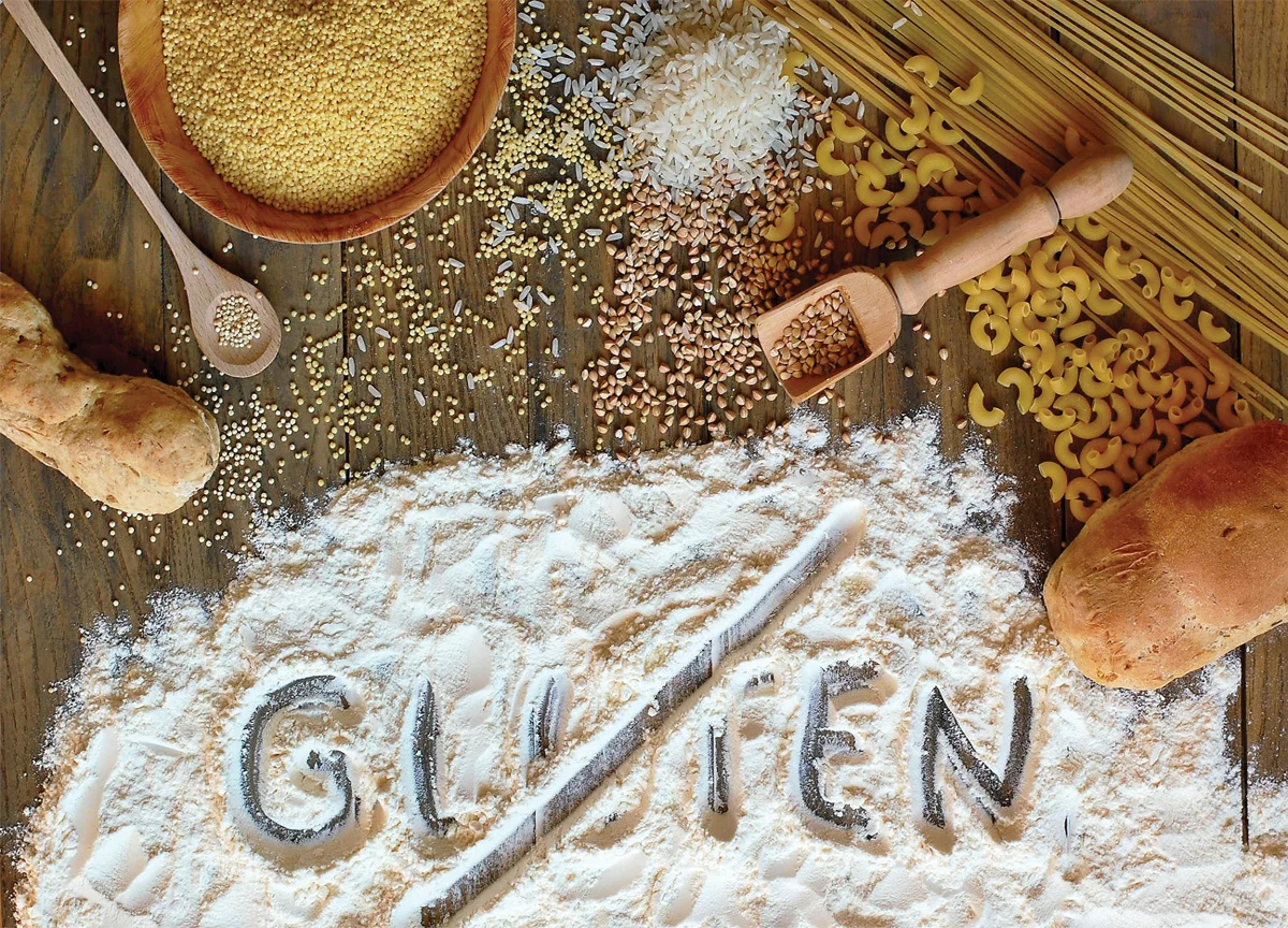 A table is covered with different grains, pasta, and flour with the word ‘gluten’ crossed out.